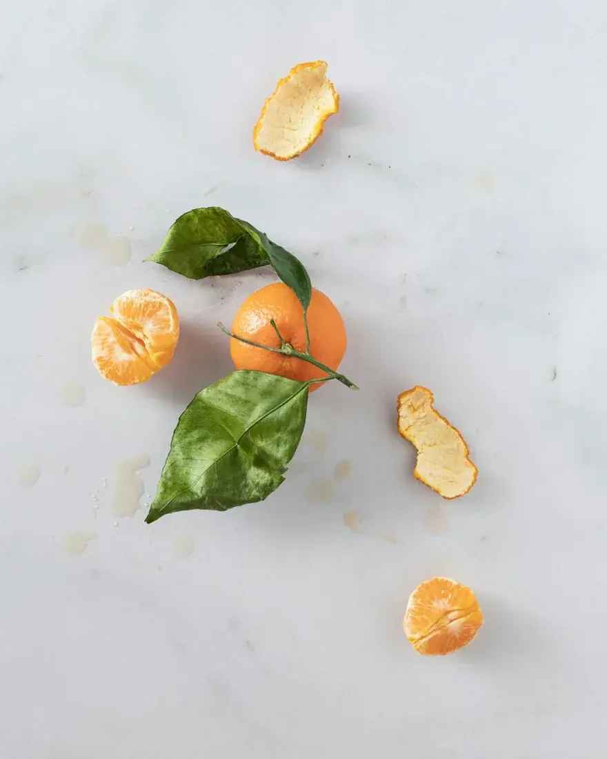 Mandarin citrus fruit, peel and leaves on a pale tabletop; representative citrus photograph, not verified Kinnow.