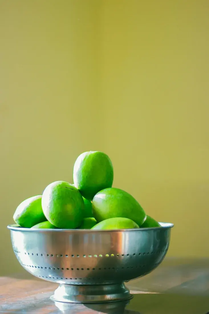 Fresh green mangoes piled in a metal colander.